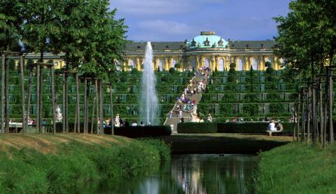 Begrünte Parkanlage mit Springbrunnen und dem Schloss Sanssouci im Sommer.