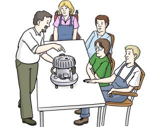 Personen sitzen an einem Tisch. Auf dem Tisch steht eine Maschine. Eine Person erklärt die Funktion der Maschine.