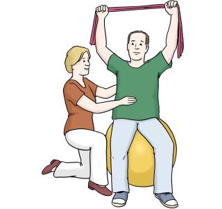 Ein Mann sitzt auf einem Sitzball. In den Händen über seinem Kopg hält er ein elastisches Band. Eine Frau kniet an seiner Seite und stützt ihn. 