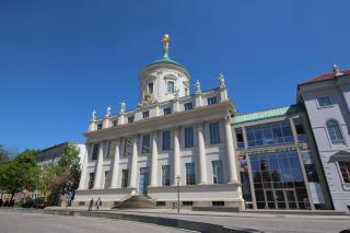Historische Außenansicht des Potsdam Museum mit verglastem Anbau des Haupteingangs. Vor dem Gebäude spazieren zwei Personen.