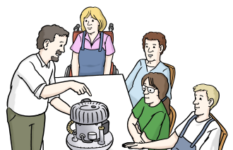 Personen sitzen an einem Tisch. Auf dem Tisch steht eine Maschine. Eine Person erklärt die Funktion der Maschine.