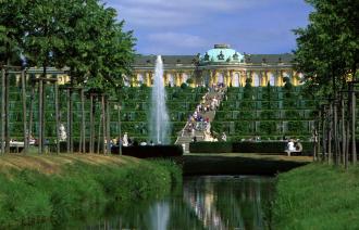 Begrünte Parkanlage mit Springbrunnen und dem Schloss Sanssouci im Sommer.