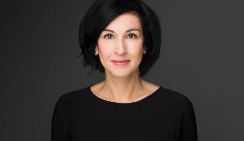 Noosha Aubel hat schwarze, schulterlange Haare. Sie trägt Lippenstift und ein schwarzes Oberteil. Sie wirkt sympathisch.