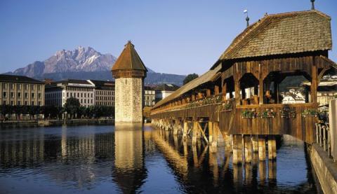Wasser mit Brücke. Im Hintergrund stehen Gebäude und ein größeres Gebirge.